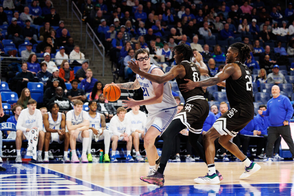 SLU's Robbie Avila handles the ball while the Billiken bench and Coach Schertz look on